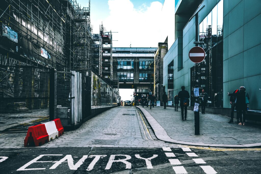 A bustling urban street with modern buildings and construction scaffolding under a clear blue sky.